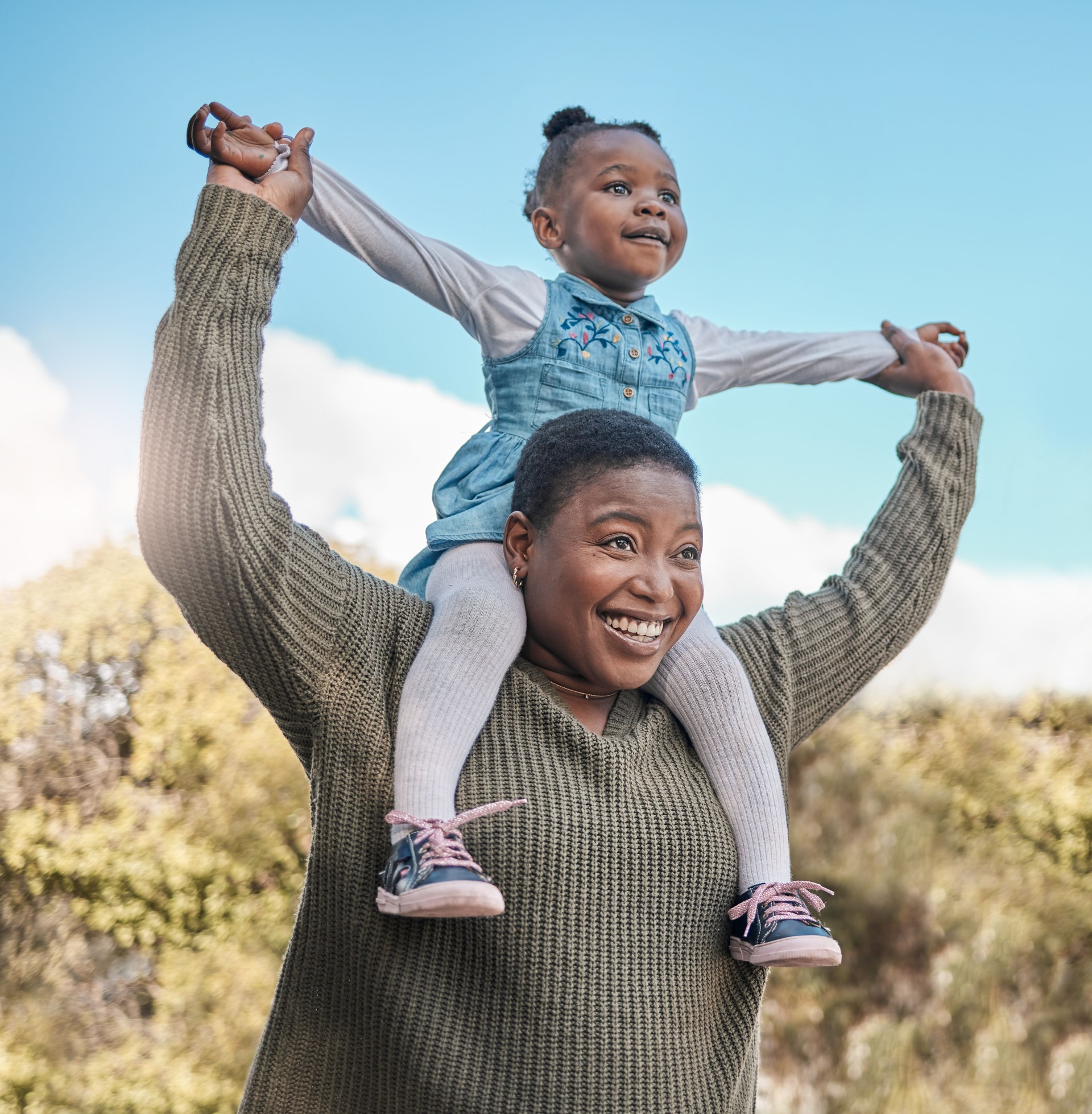 Shot of a mother carrying her daughter on her shoulders outdoors